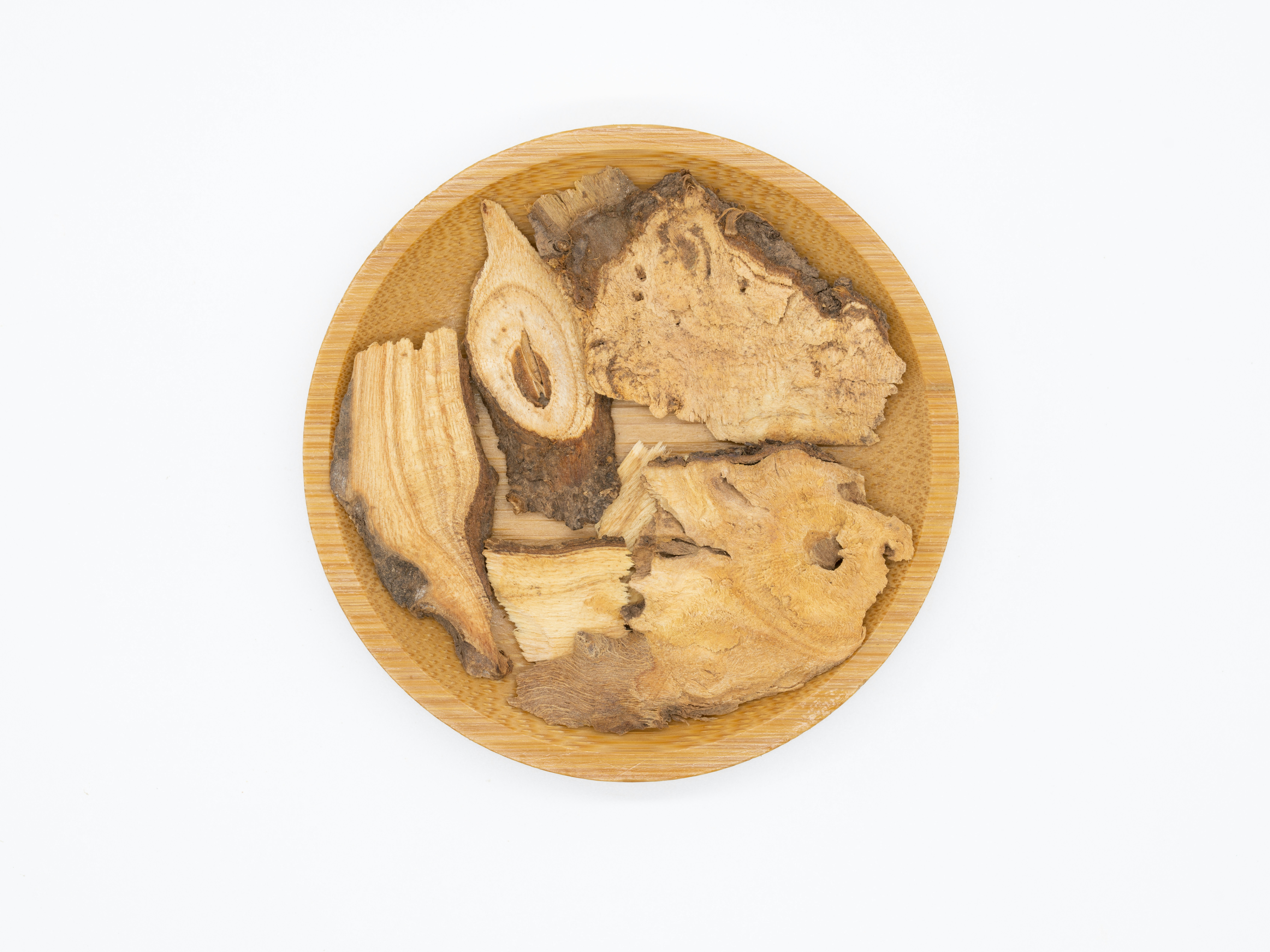 Dried herbs, roots, and medicinal plants arranged in wooden bowls with mortar and pestle in warm light