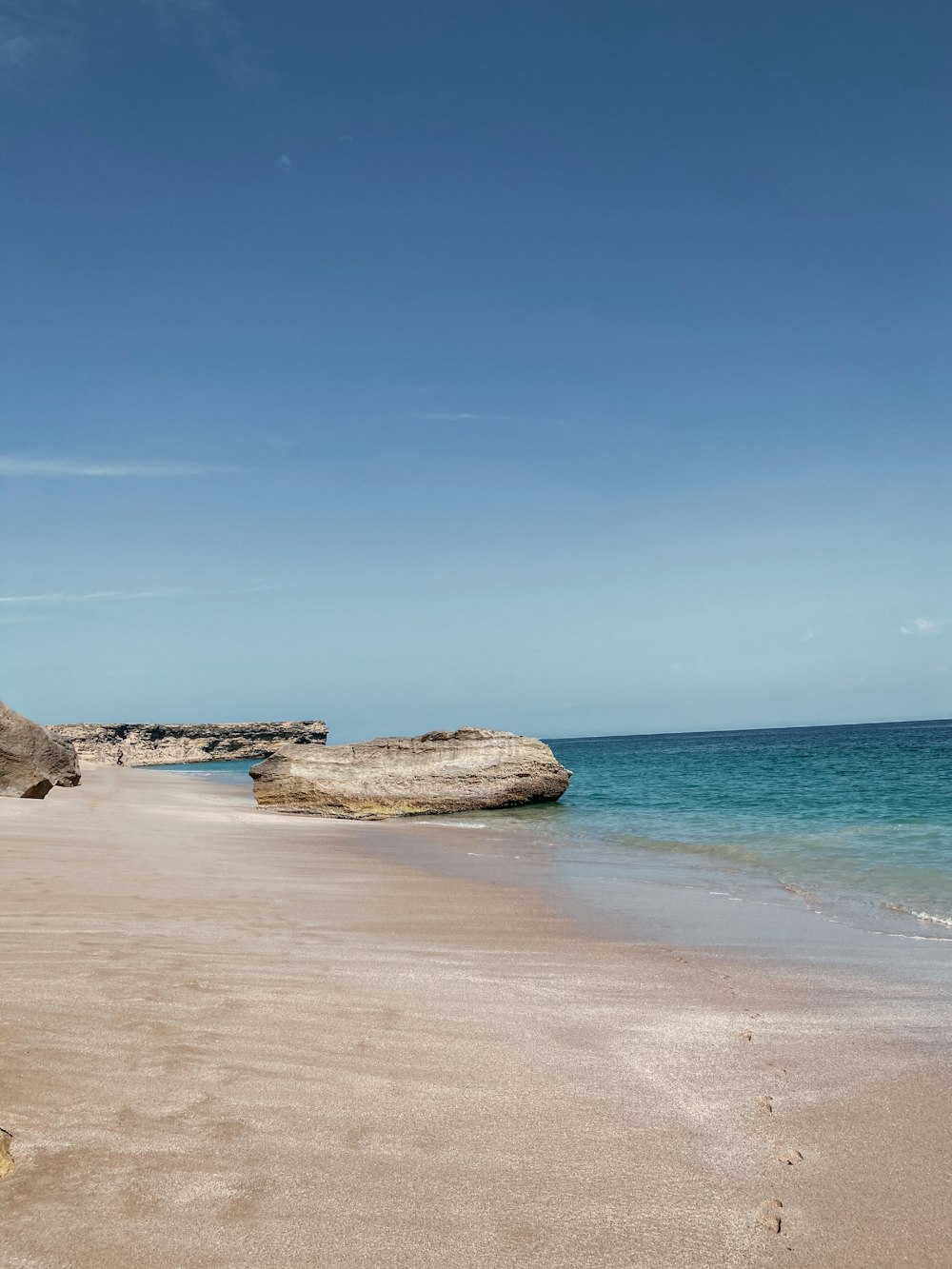 a sandy beach next to the ocean under a blue sky