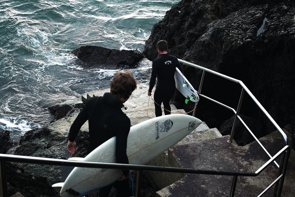 two surfers walking up a set of stairs towards the ocean