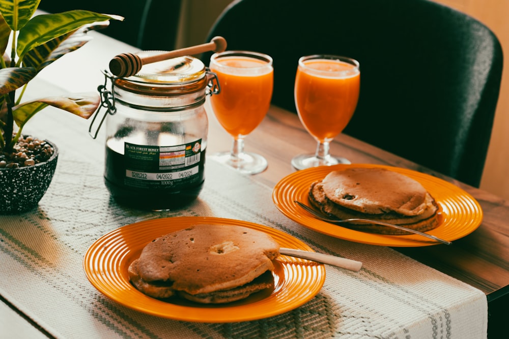 a table with two plates of pancakes and two glasses of orange juice