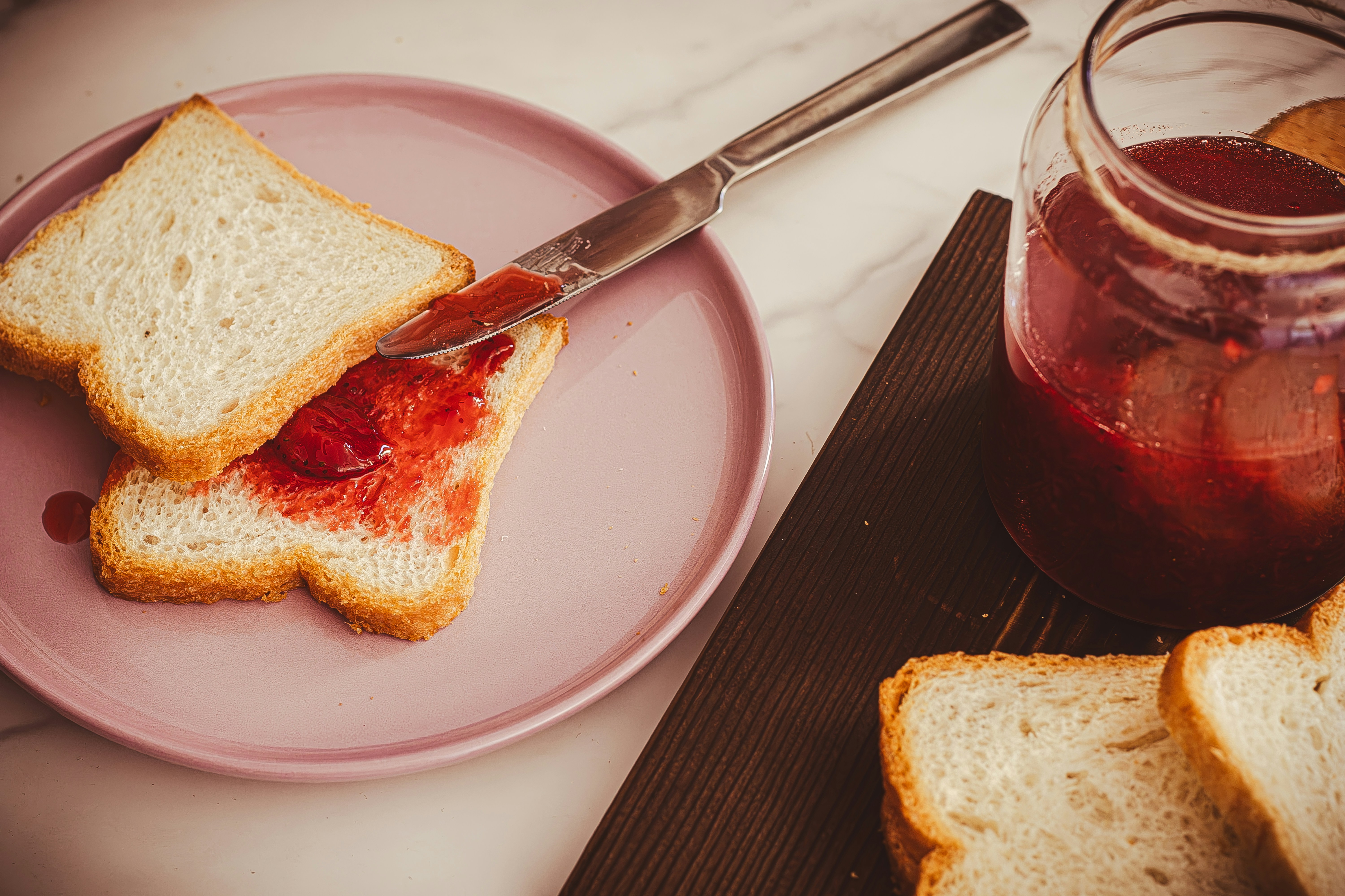 a piece of bread on a pink plate next to a jar of jelly, 