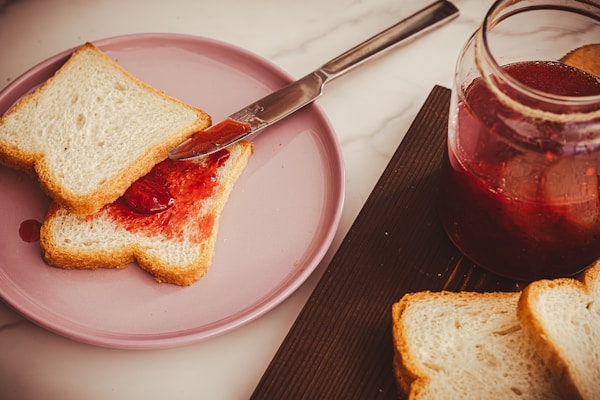 A piece of bread on a pink plate next to a jar of jelly