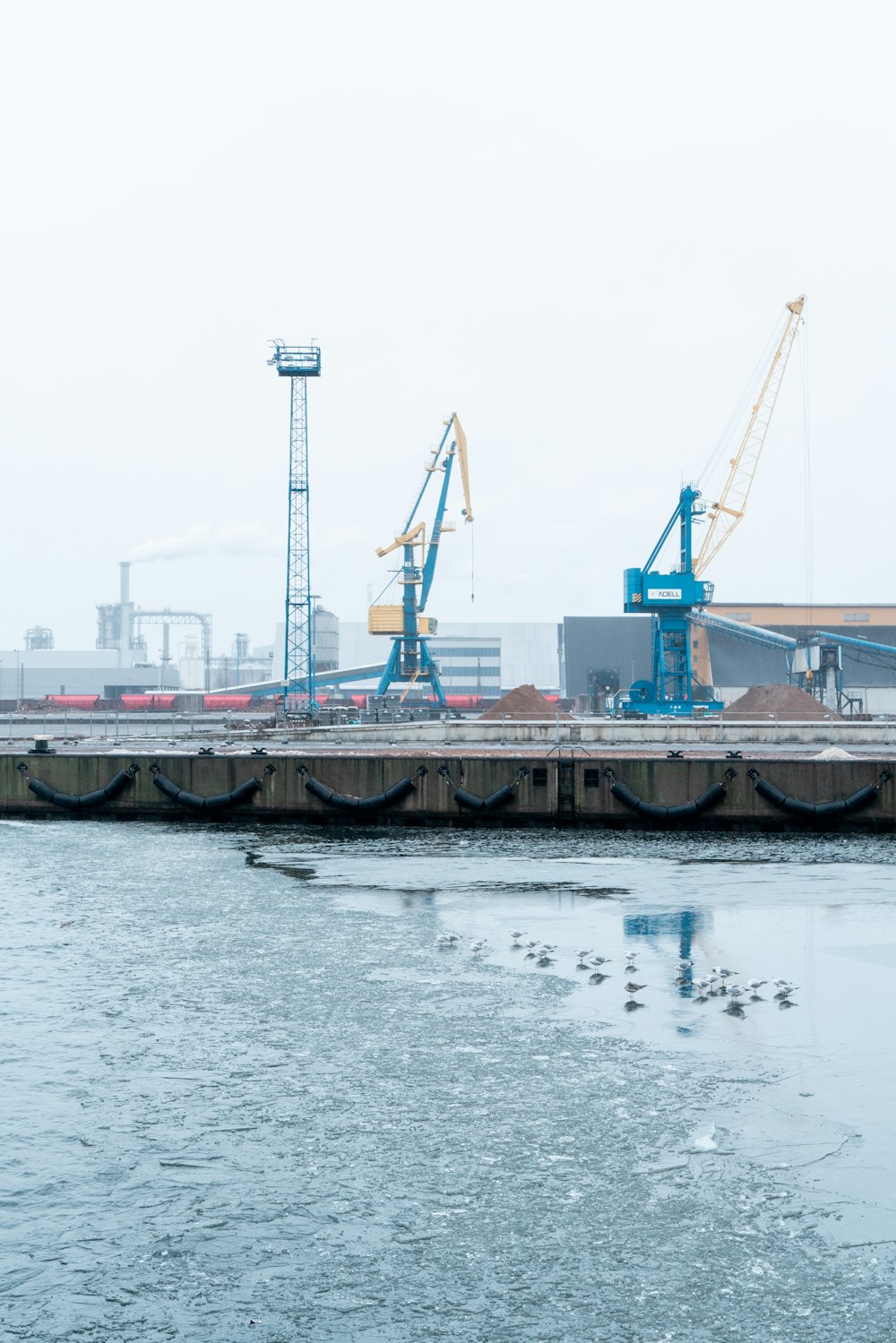 a body of water with a dock and cranes in the background