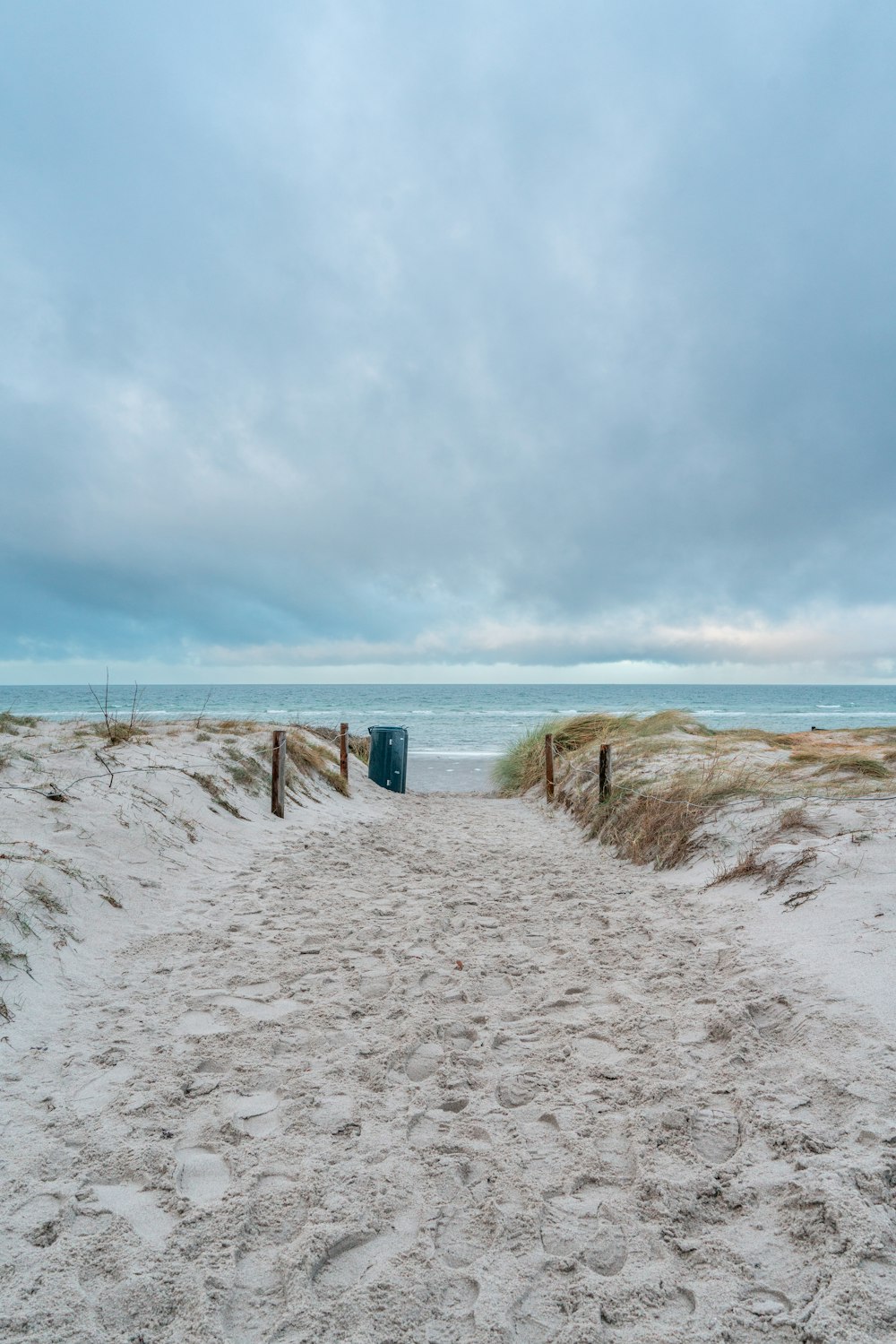 a sandy path leading to the beach with a trash can in the distance