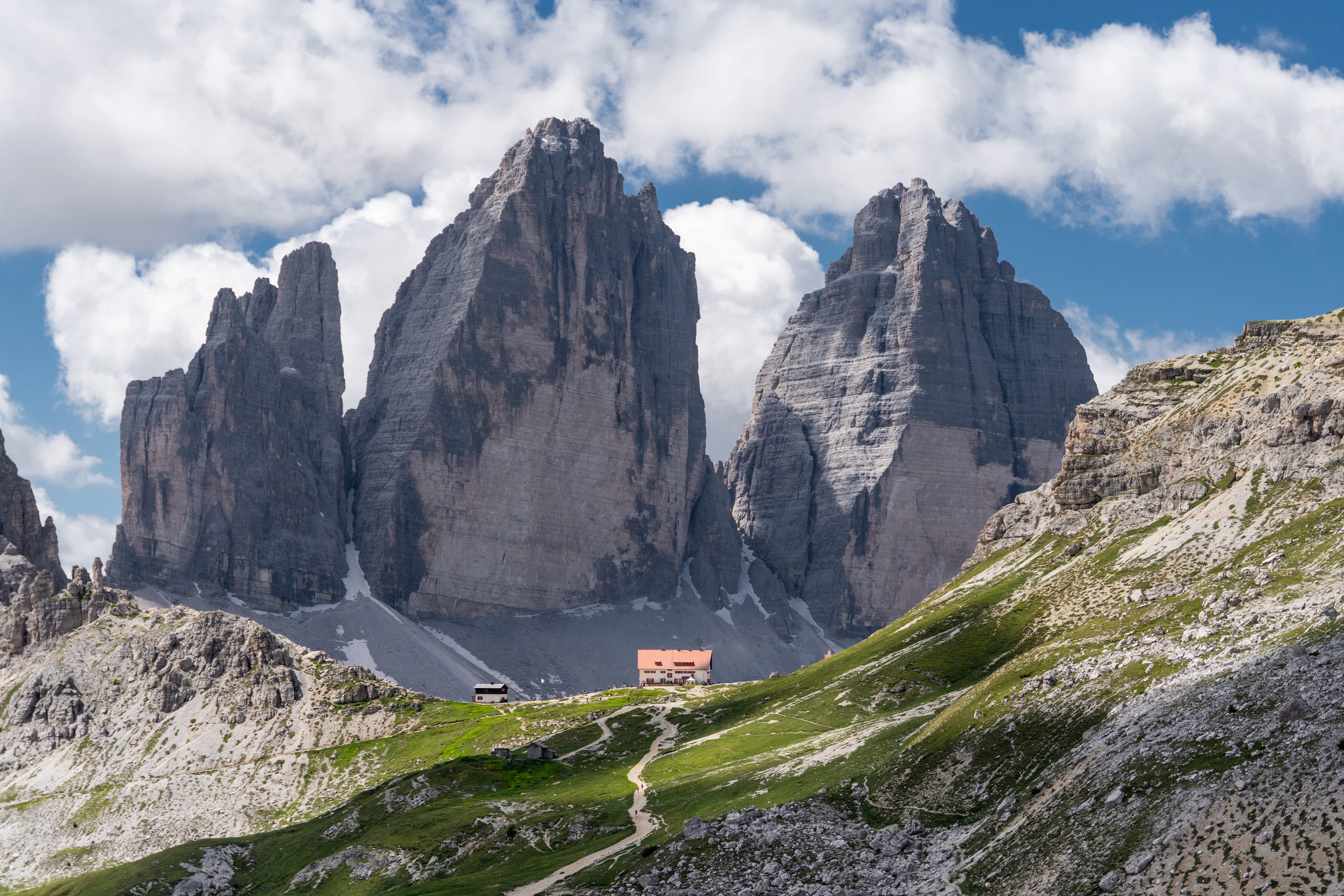 The Tre Cime di Lavaredo above a mountain hut and green slopes on a summer afternoon