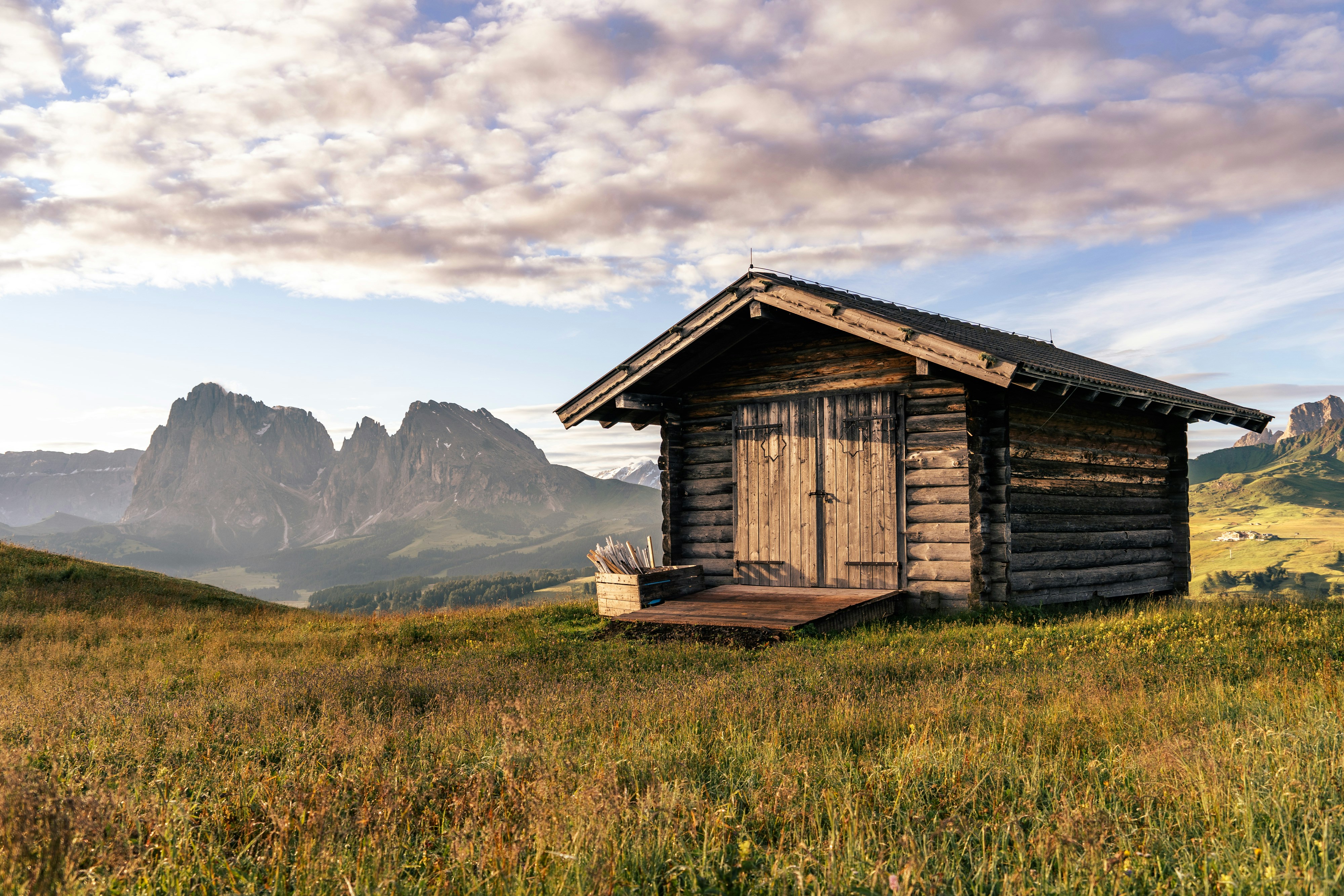 a small cabin in a field with mountains in the background, Sunrise at the Alpe di Siusi in the Italian Dolomites