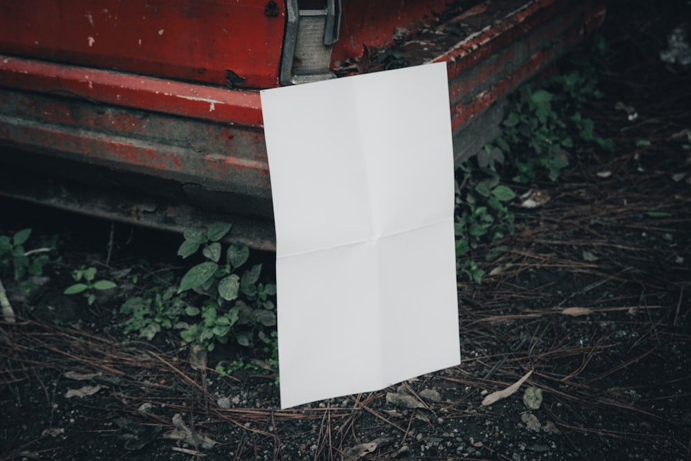 a piece of white paper sitting on the ground next to a red car