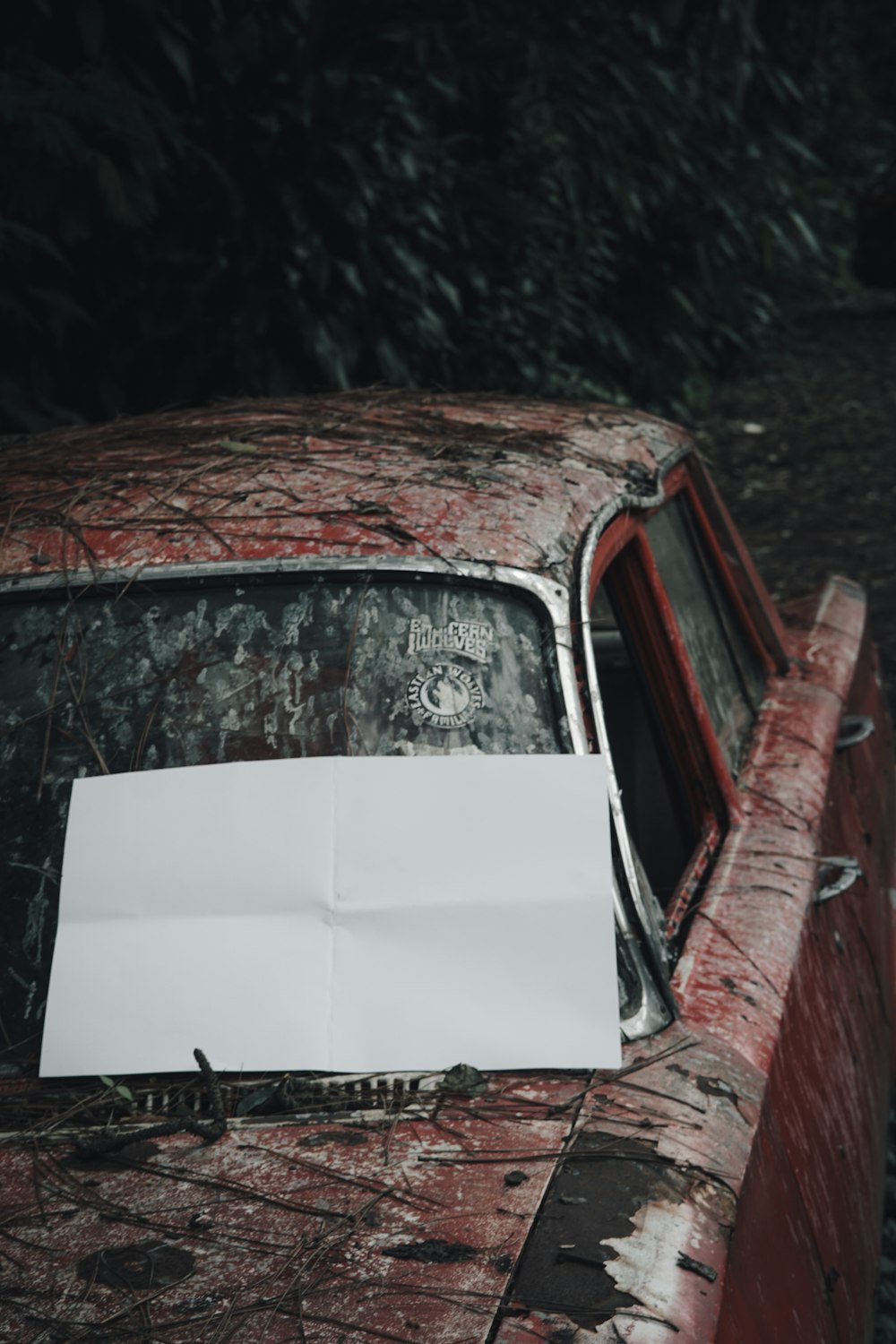 an old rusted out car with a piece of paper on the hood
