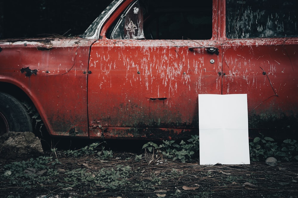 an old red car with a white sheet of paper stuck to the side of it