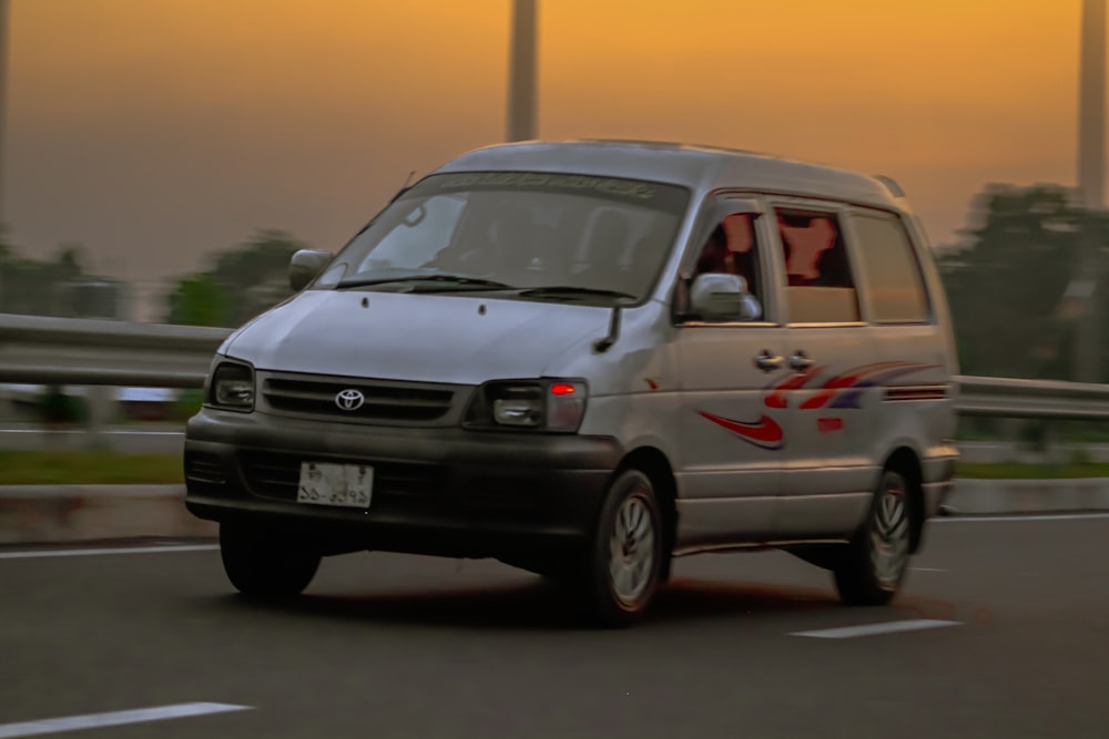 a silver van driving down a street next to tall buildings