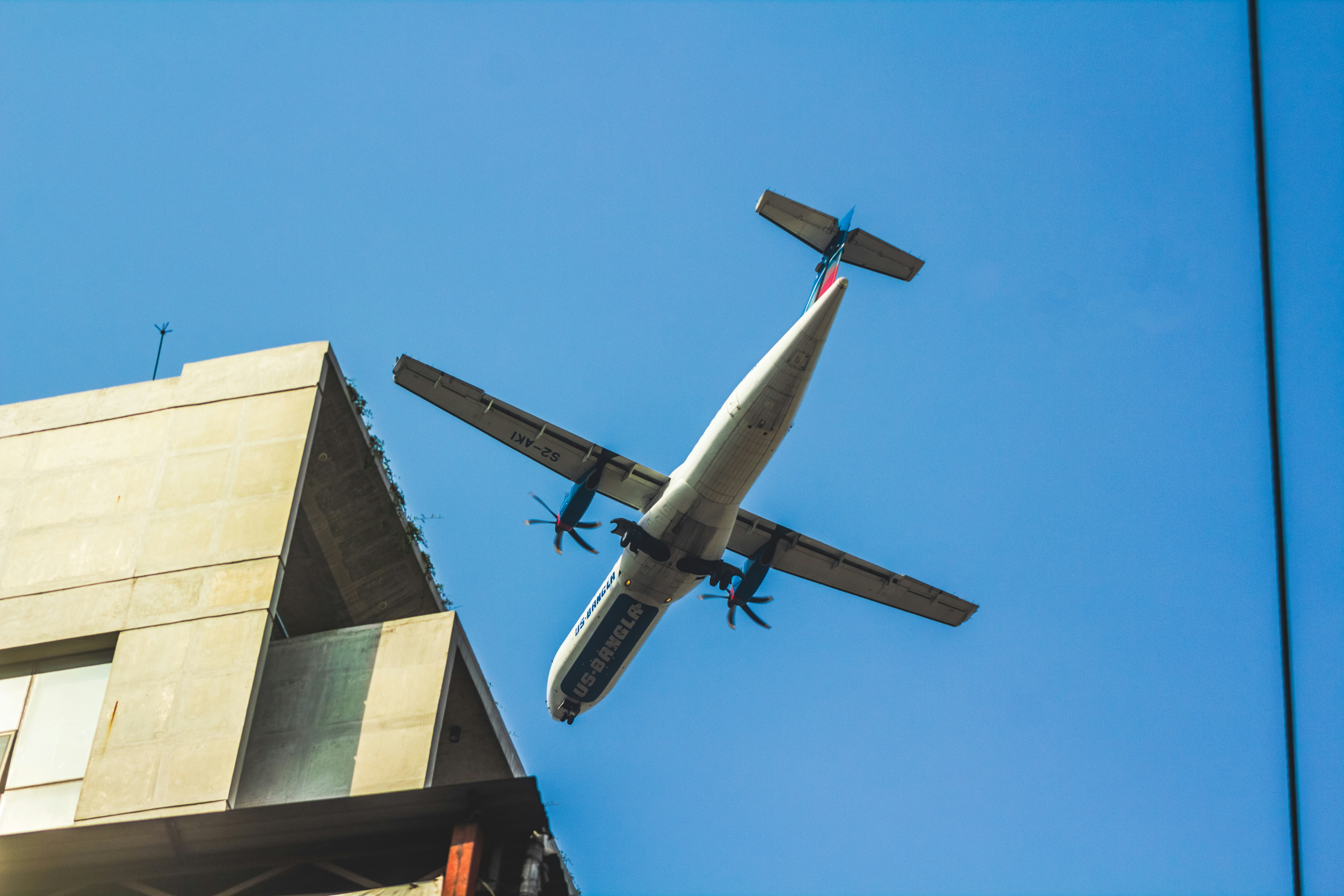 an airplane flying over a building in the sky, AT76 operated by US-Bangla Airlines.