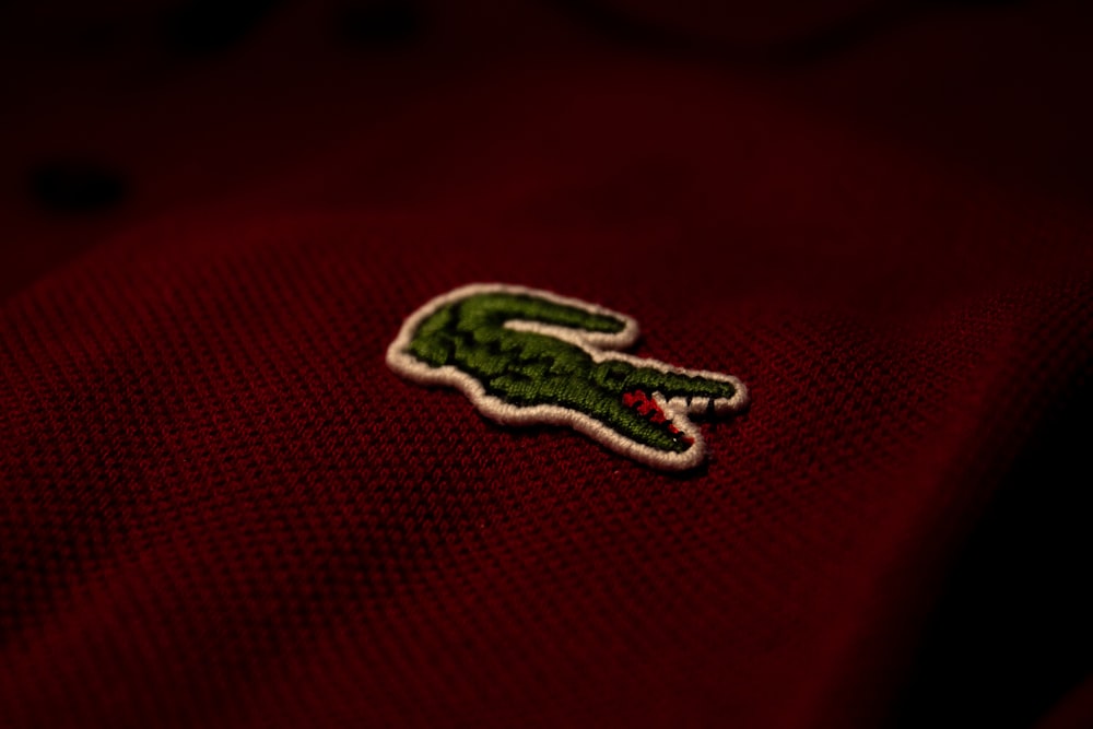 Un primer plano de un polo rojo con un caimán verde bordado en él