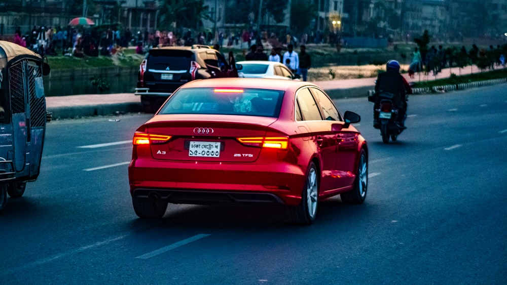 a red car driving down a street next to a motorcycle