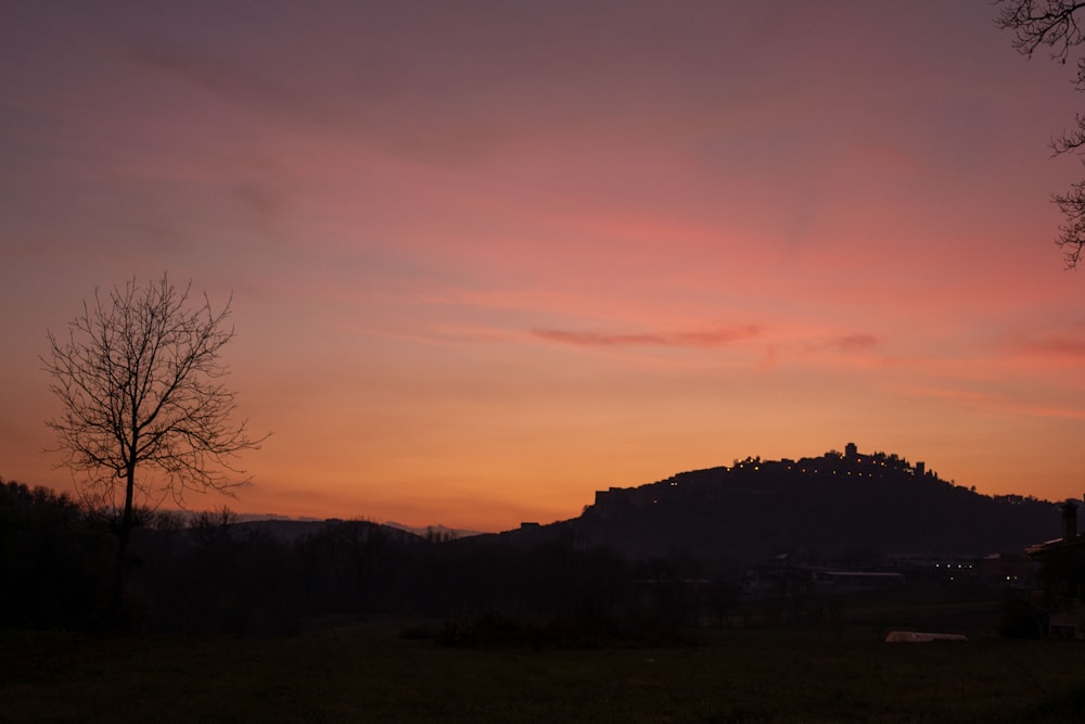 a sunset view of a hill with trees in the foreground