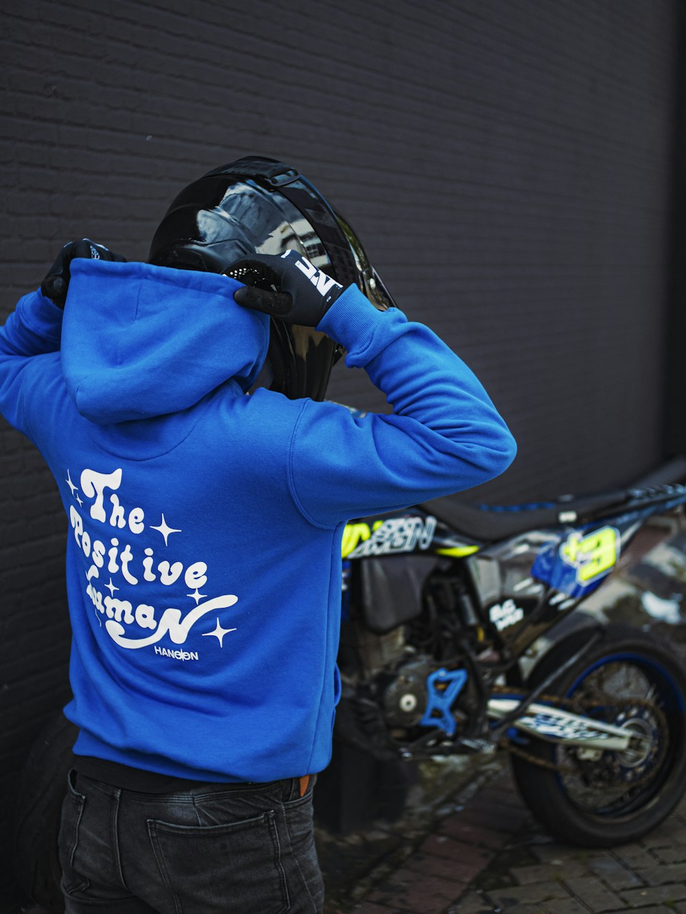 a man in a blue hoodie stands next to a motorcycle
