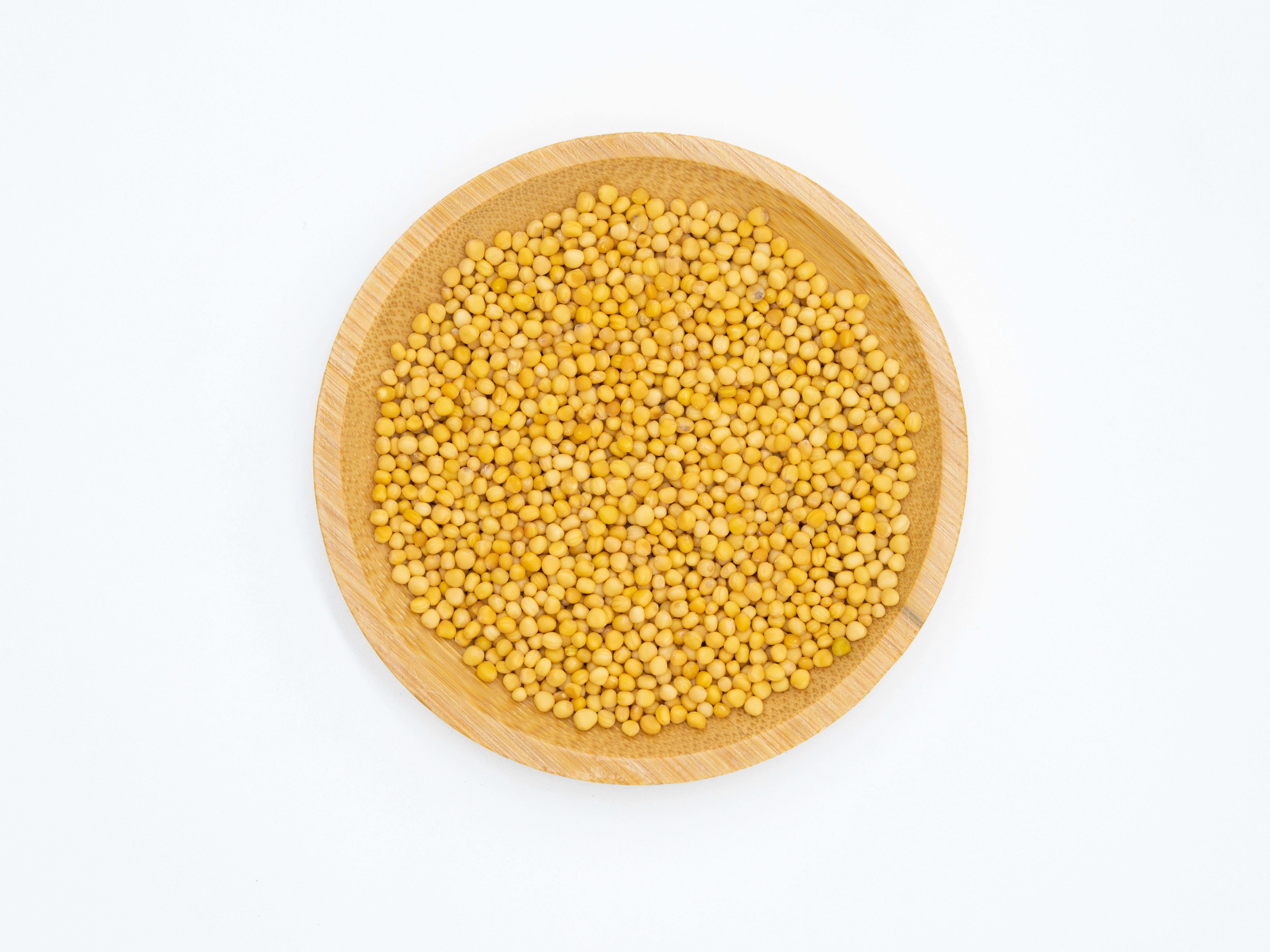 Yellow mustard seeds scattered on wooden surface, bright natural lighting