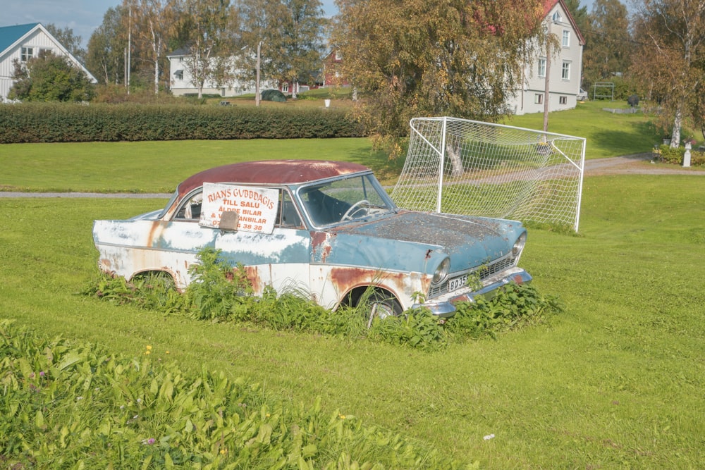 um carro velho sentado em um campo ao lado de um gol de futebol