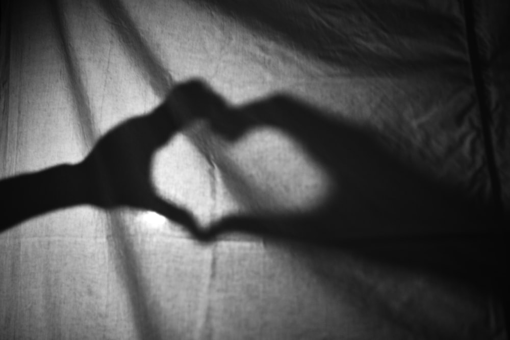 a shadow of a person making a heart with their hands