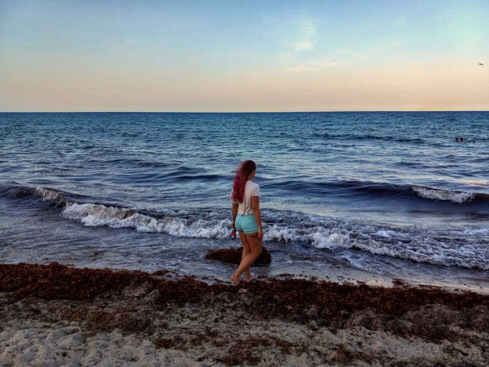 a woman walking along a beach next to the ocean