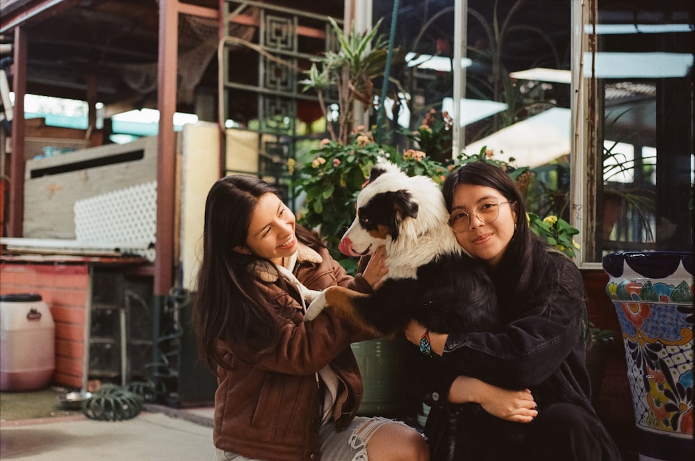 two women sitting on a bench petting a dog