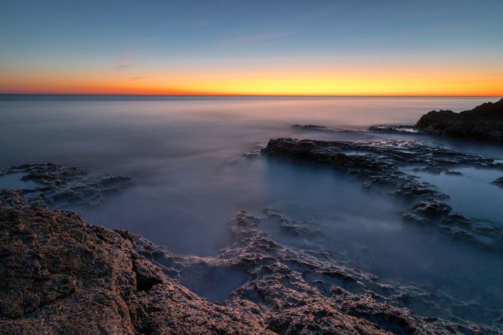 the sun is setting over the water and rocks