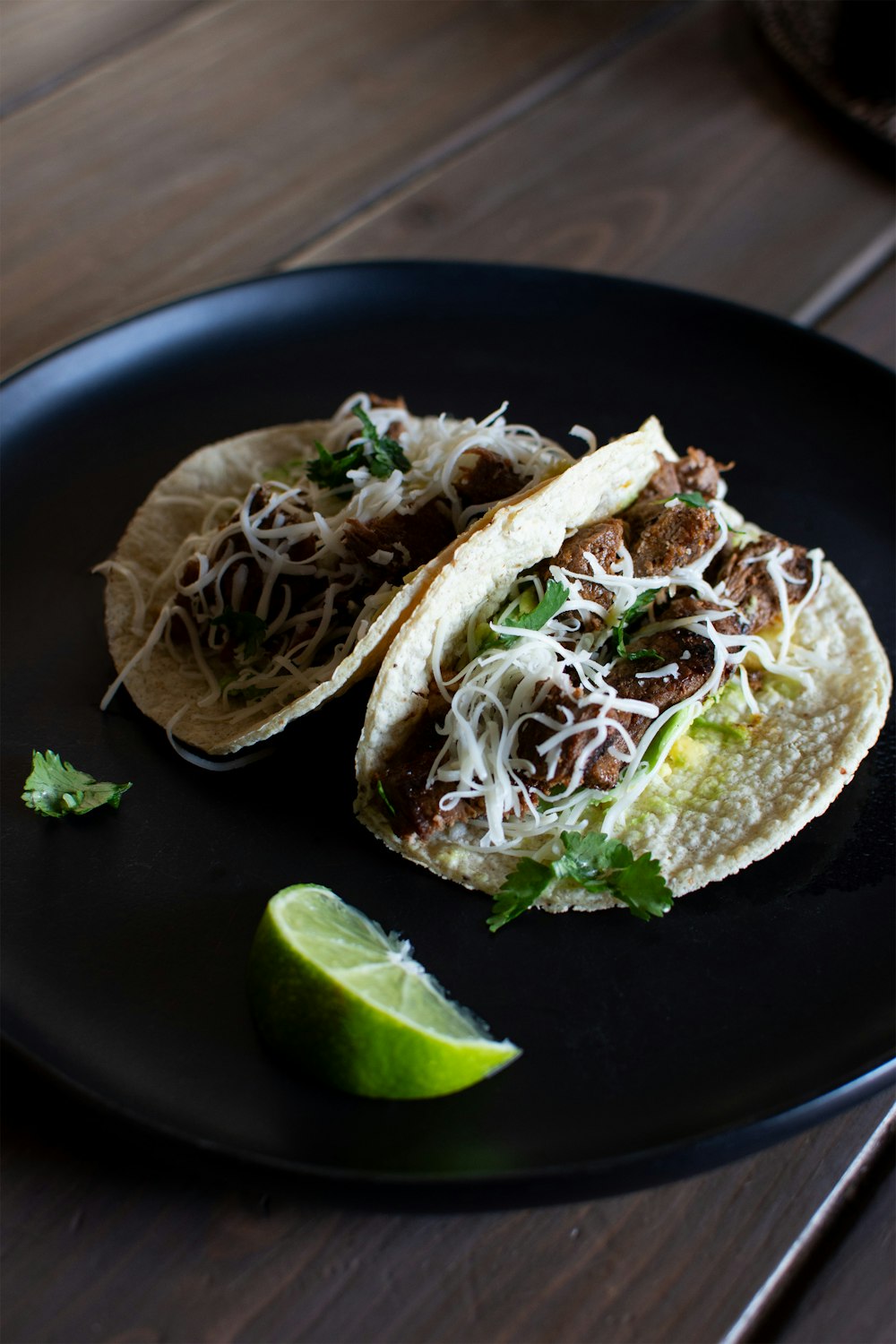 two tacos on a black plate with a lime