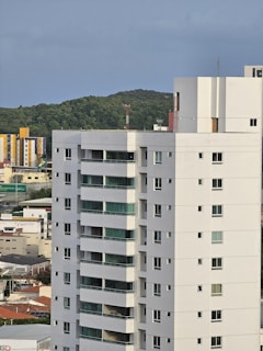a tall white building sitting next to a lush green hillside