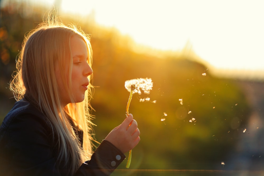 a young girl blowing a dandelion in the sun