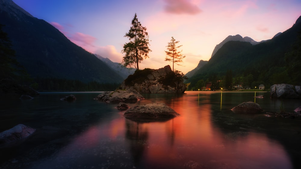 a lake surrounded by mountains and trees at sunset