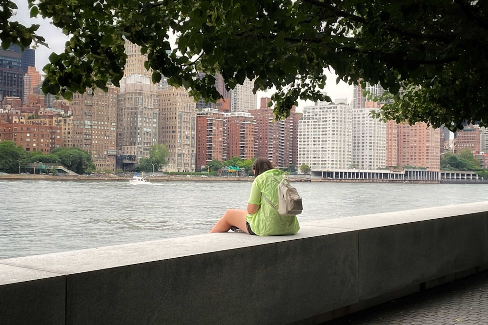 a person sitting on a concrete wall near a body of water