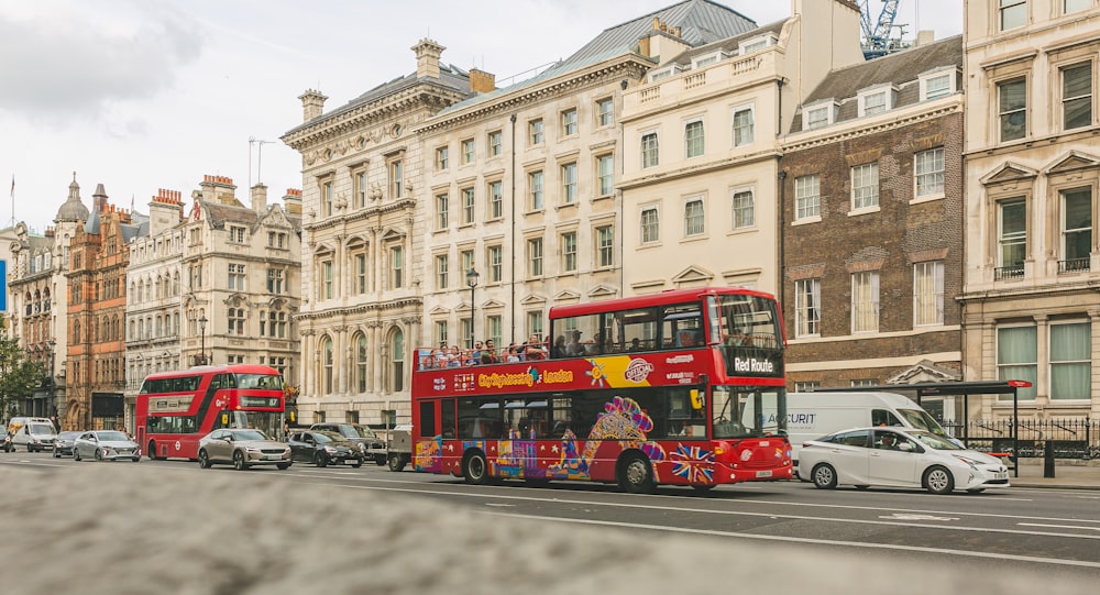 a red double decker bus driving down a street next to tall buildings