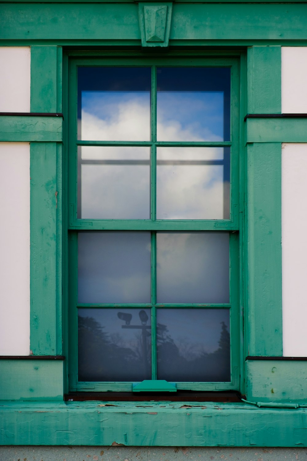 una finestra verde con un cielo nuvoloso che si riflette in essa
