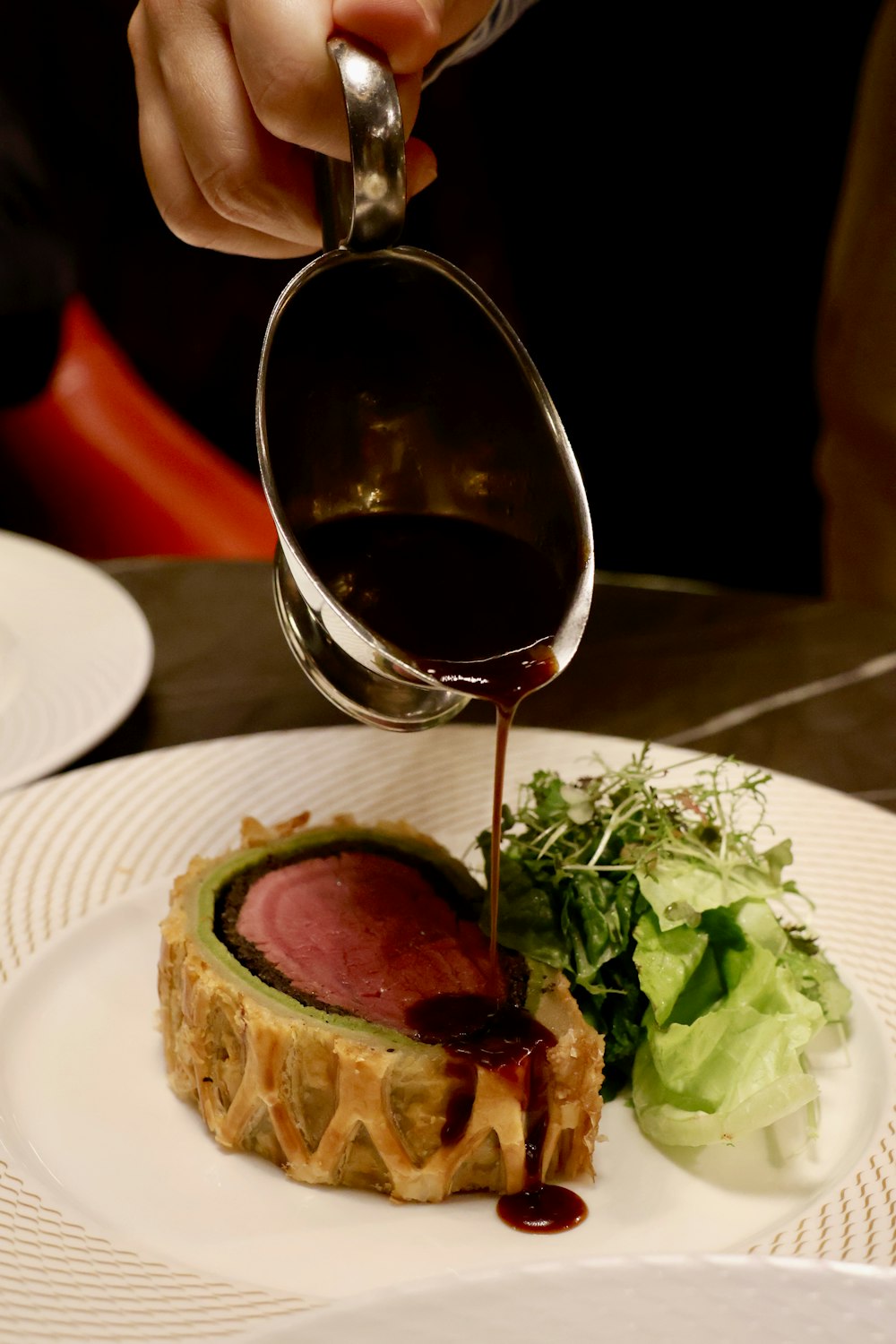 a person pouring sauce on a piece of meat