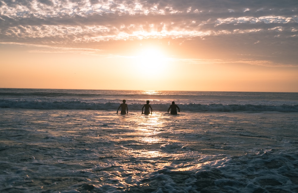 Drei Surfer gehen bei Sonnenuntergang ins Meer