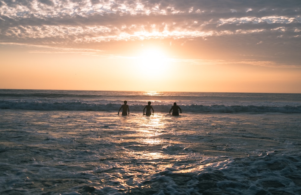 three surfers walking into the ocean at sunset