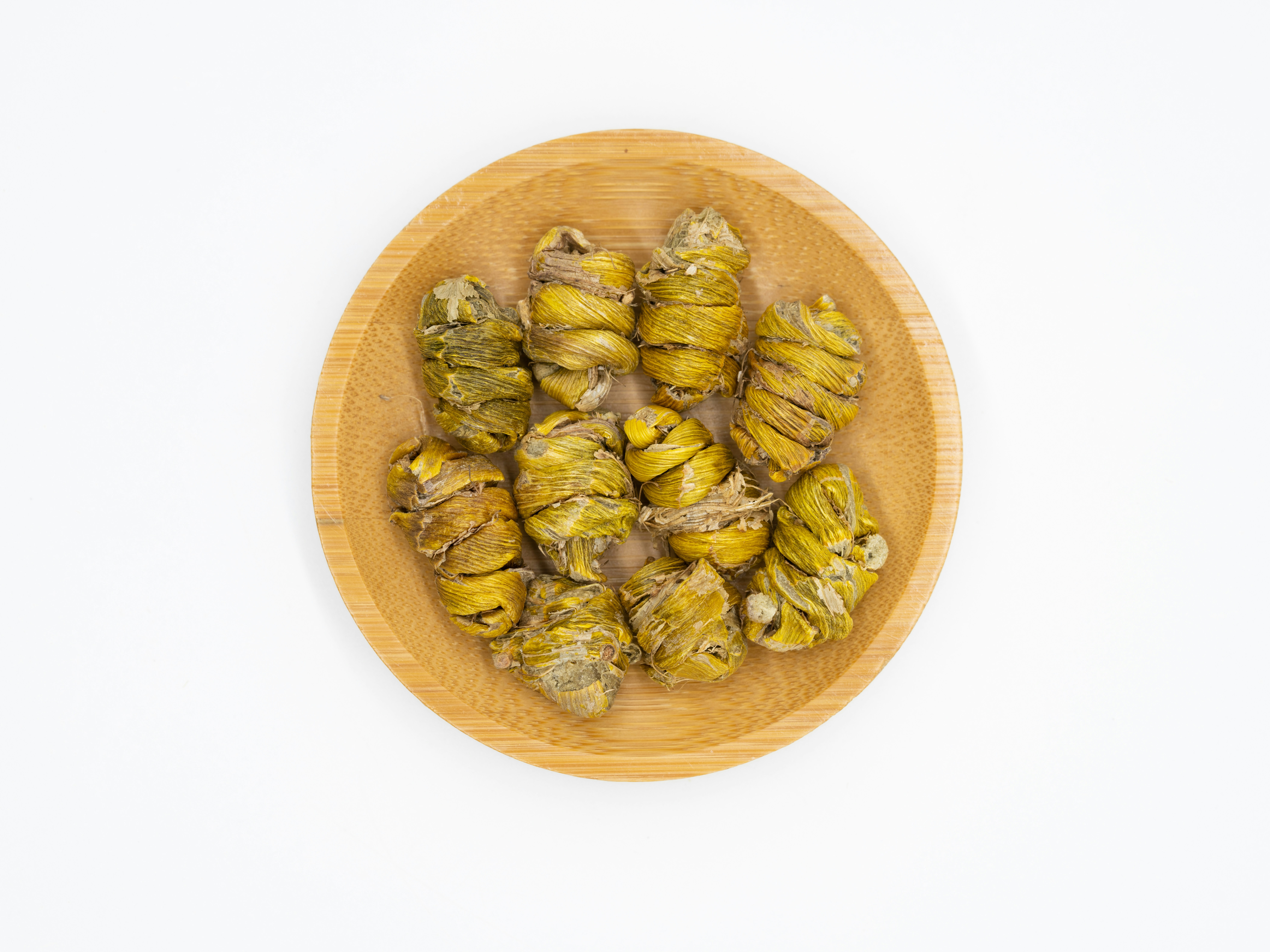 Loose leaf herbal tea in a wooden bowl with dried flowers and herbs scattered on a light background