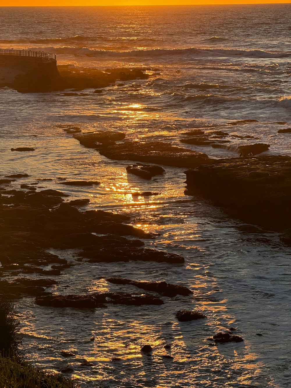 the sun is setting over the ocean with rocks in the foreground