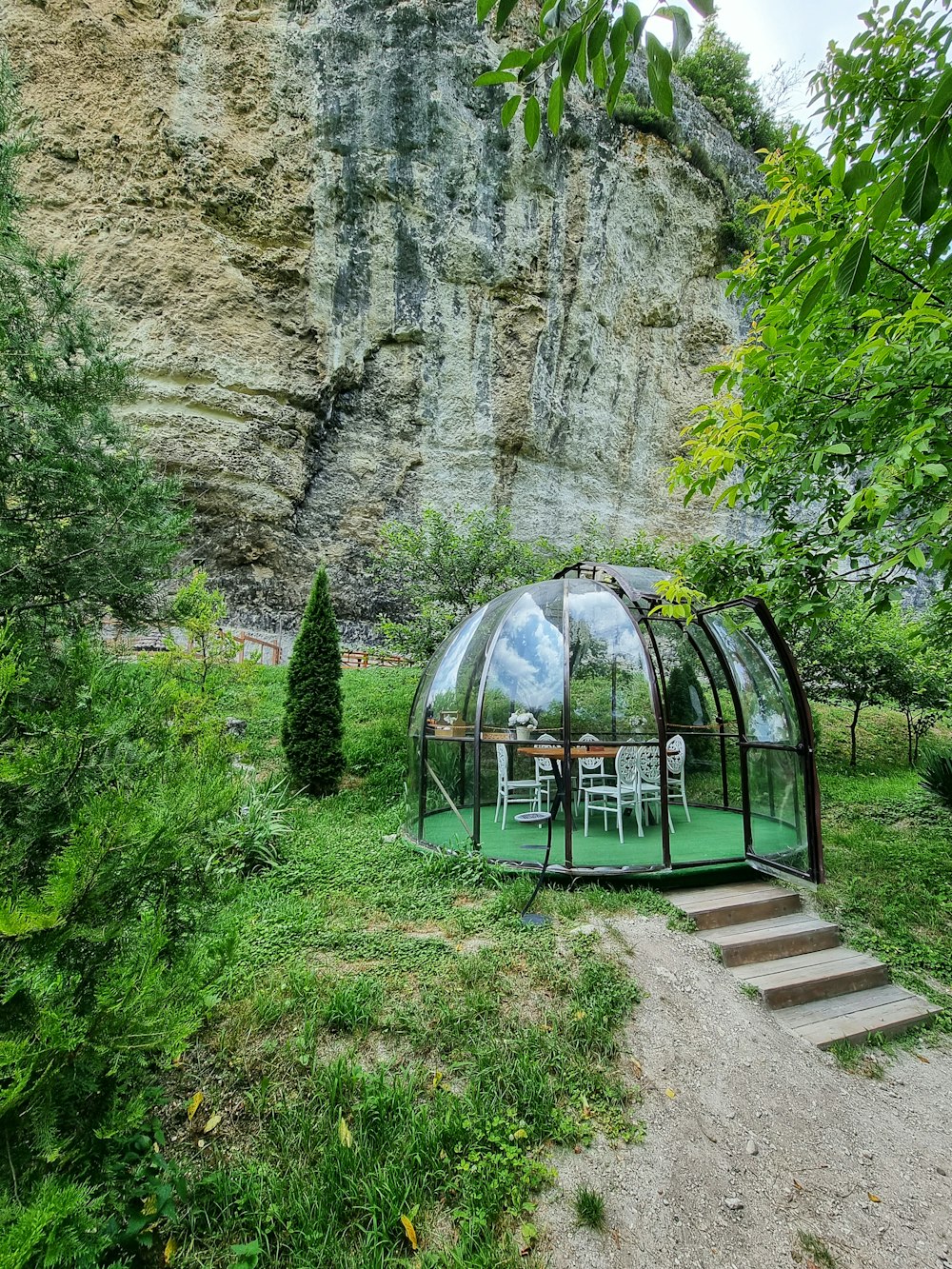 a glass house in the middle of a lush green field