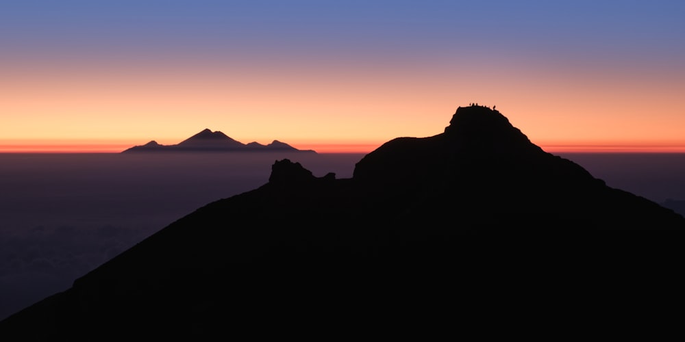 una silueta de una montaña con una puesta de sol en el fondo