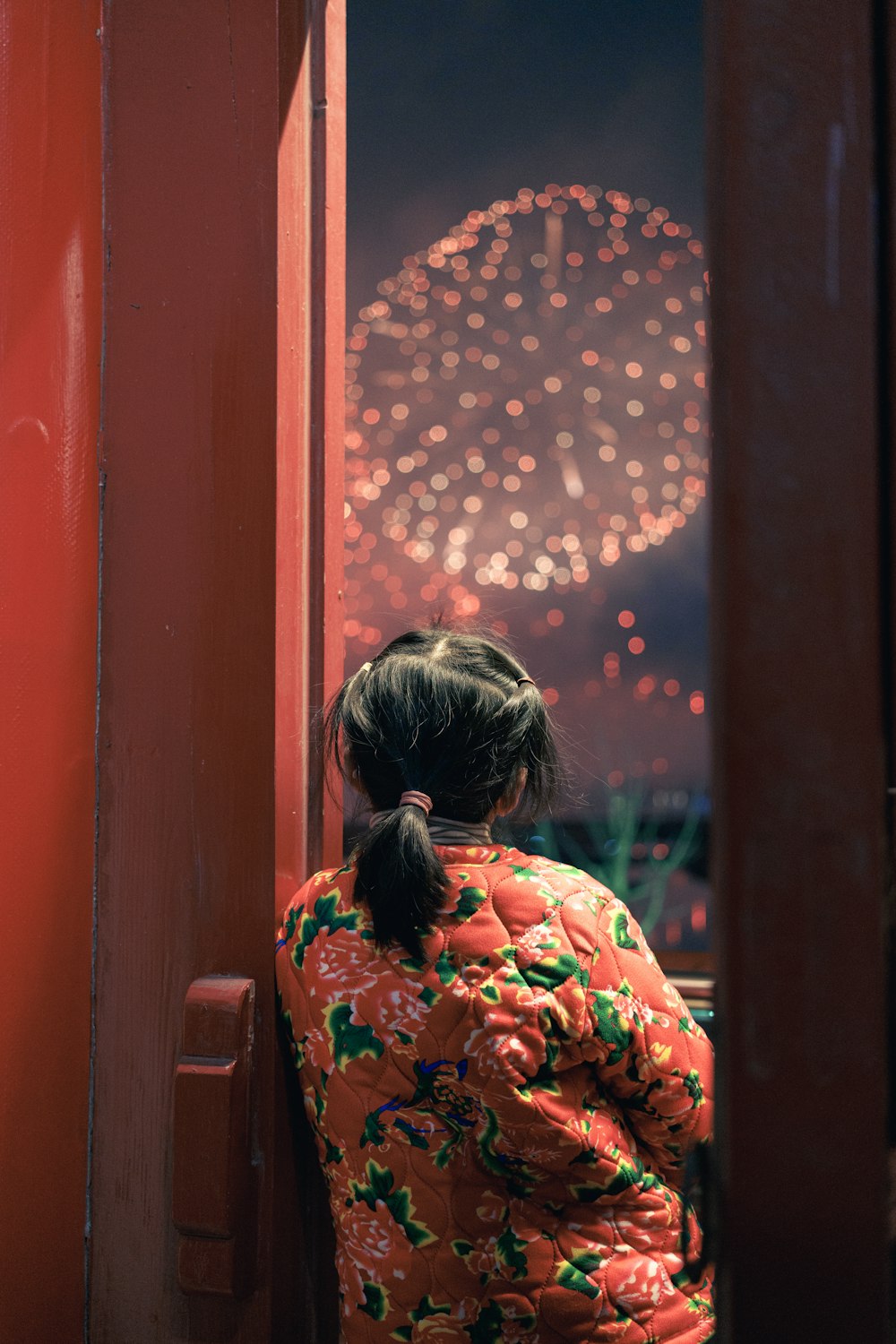 a little girl looking out a window at fireworks