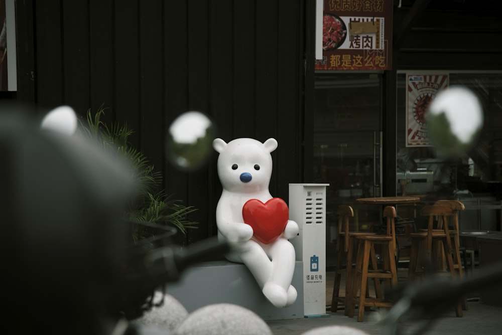 un grand ours en peluche blanc tenant un cœur rouge