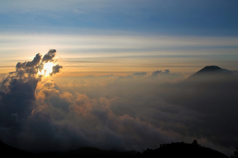 the sun peeking through the clouds above a mountain