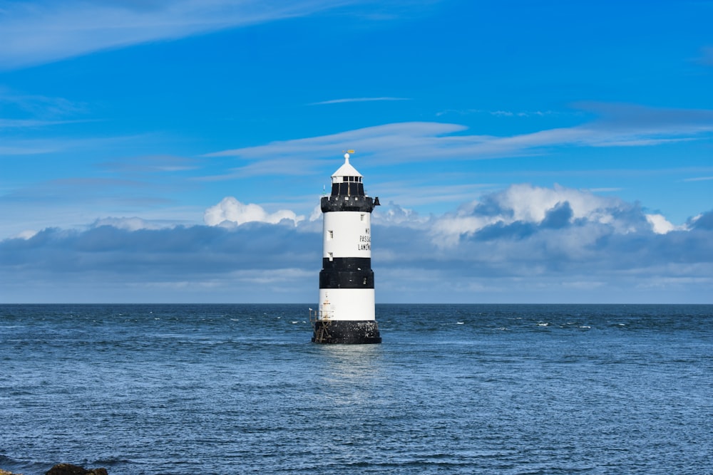 a black and white lighthouse sitting in the middle of the ocean