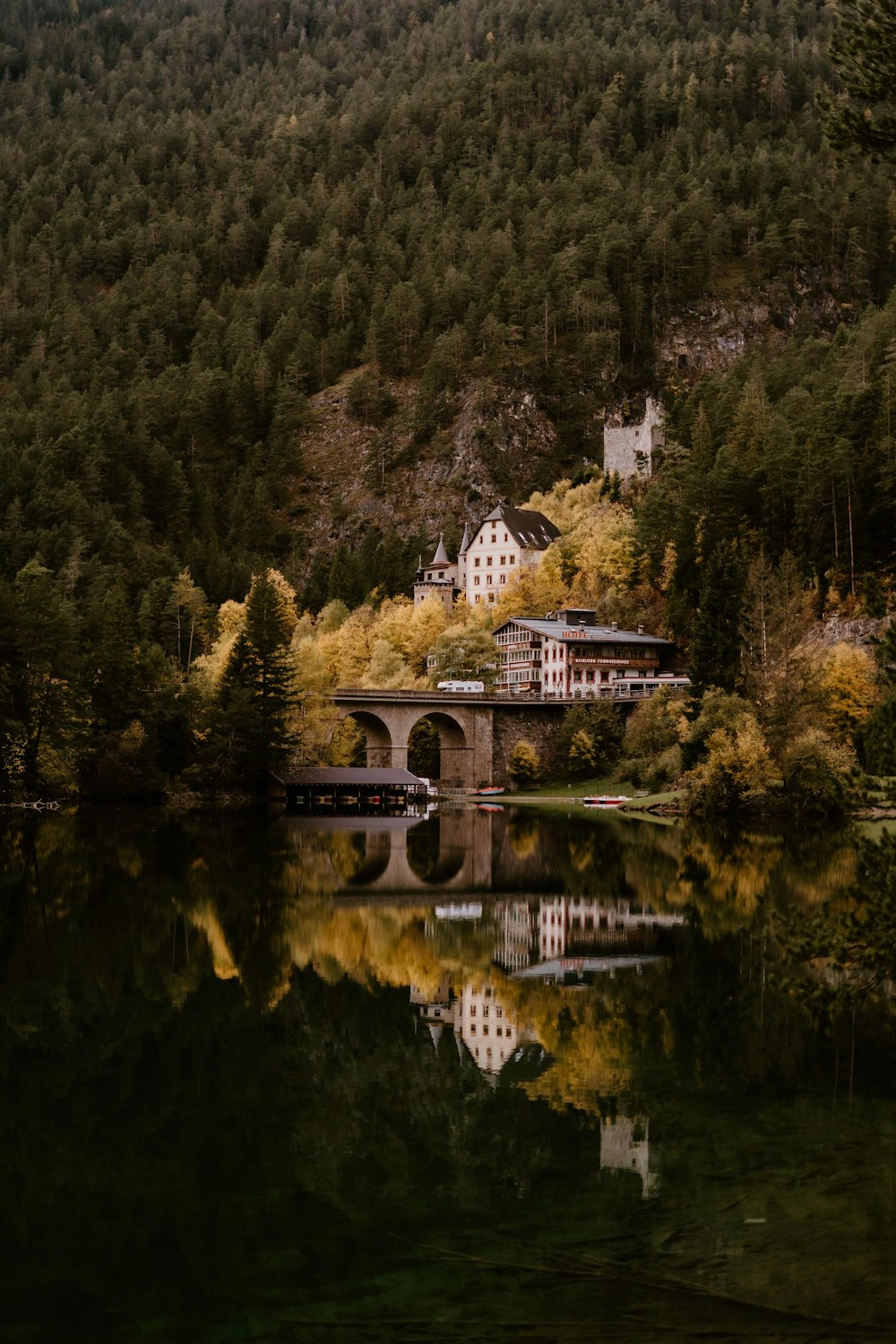 a house sitting on top of a lush green hillside next to a lake