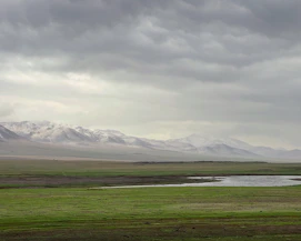 a field with a river and mountains in the background