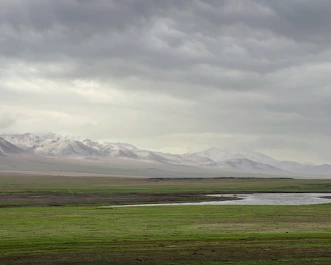 a field with a river and mountains in the background