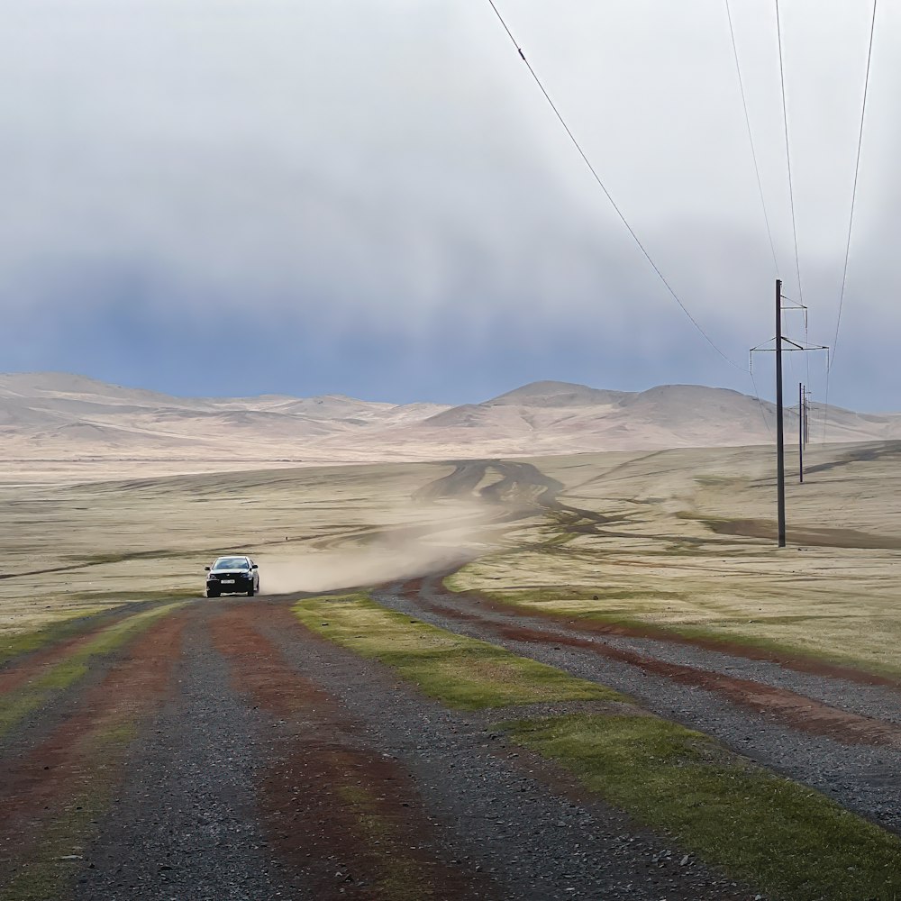 a car driving down a dirt road in the middle of nowhere