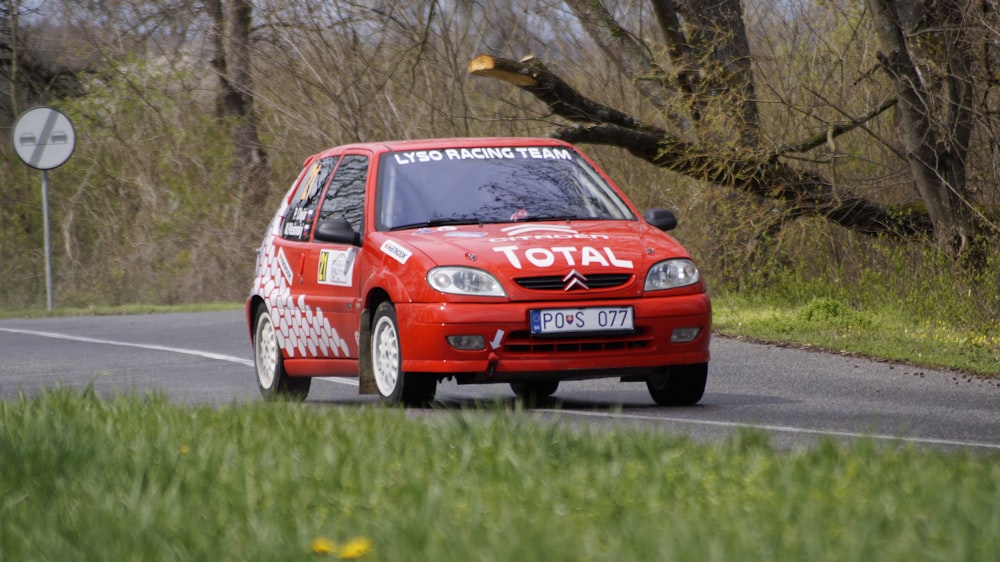 a small red car driving down a country road