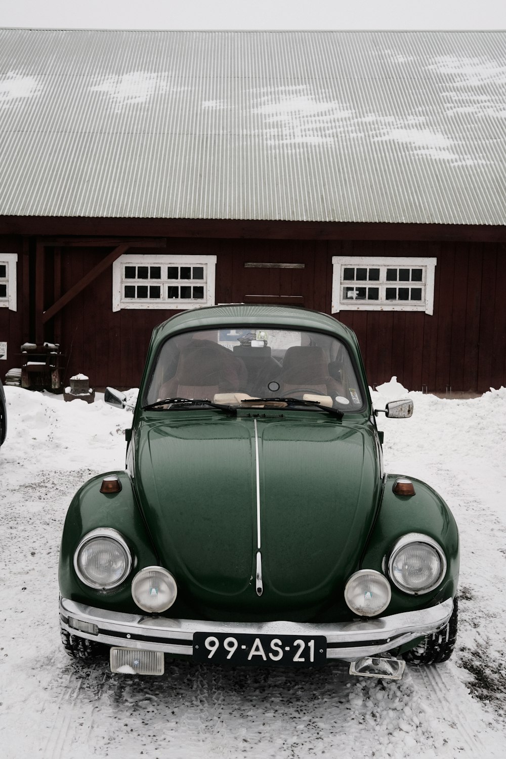 a green car parked in front of a barn