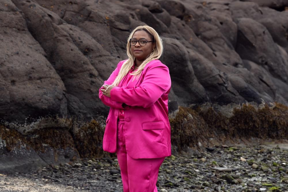 a woman in a pink suit standing on a rocky beach
